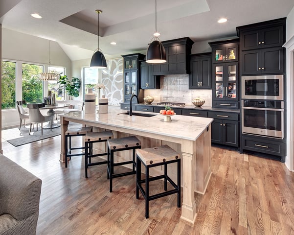 Modern kitchen design by Dusty Rhodes Homes featuring navy cabinetry, a light wood island with marble countertop, black pendant lights, and stainless steel built-in appliances.