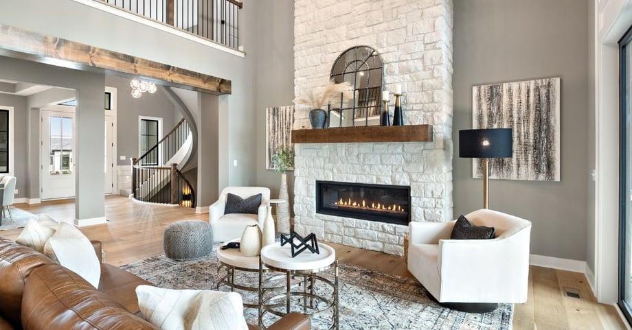 Two-story great room in a Dusty Rhodes custom home in the Kansas City area, featuring a stone fireplace with wood mantel, curved staircase, leather sectional, and white swivel accent chairs.