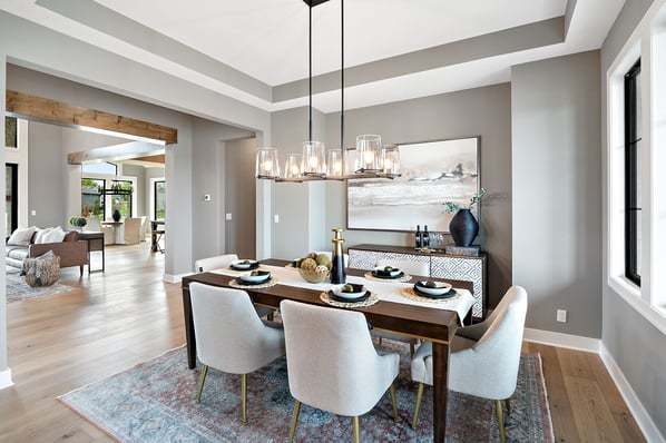 Formal dining room in a Dusty Rhodes custom home in the Kansas City area, featuring a wood dining table with upholstered chairs, a glass cylinder chandelier, and an open view to the living room.