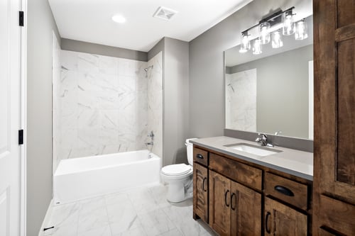 A remodeled master bathroom in an Overland Park, Kansas, home with a porcelain vanity, wooden cabinets, and marble shower and floor tiles