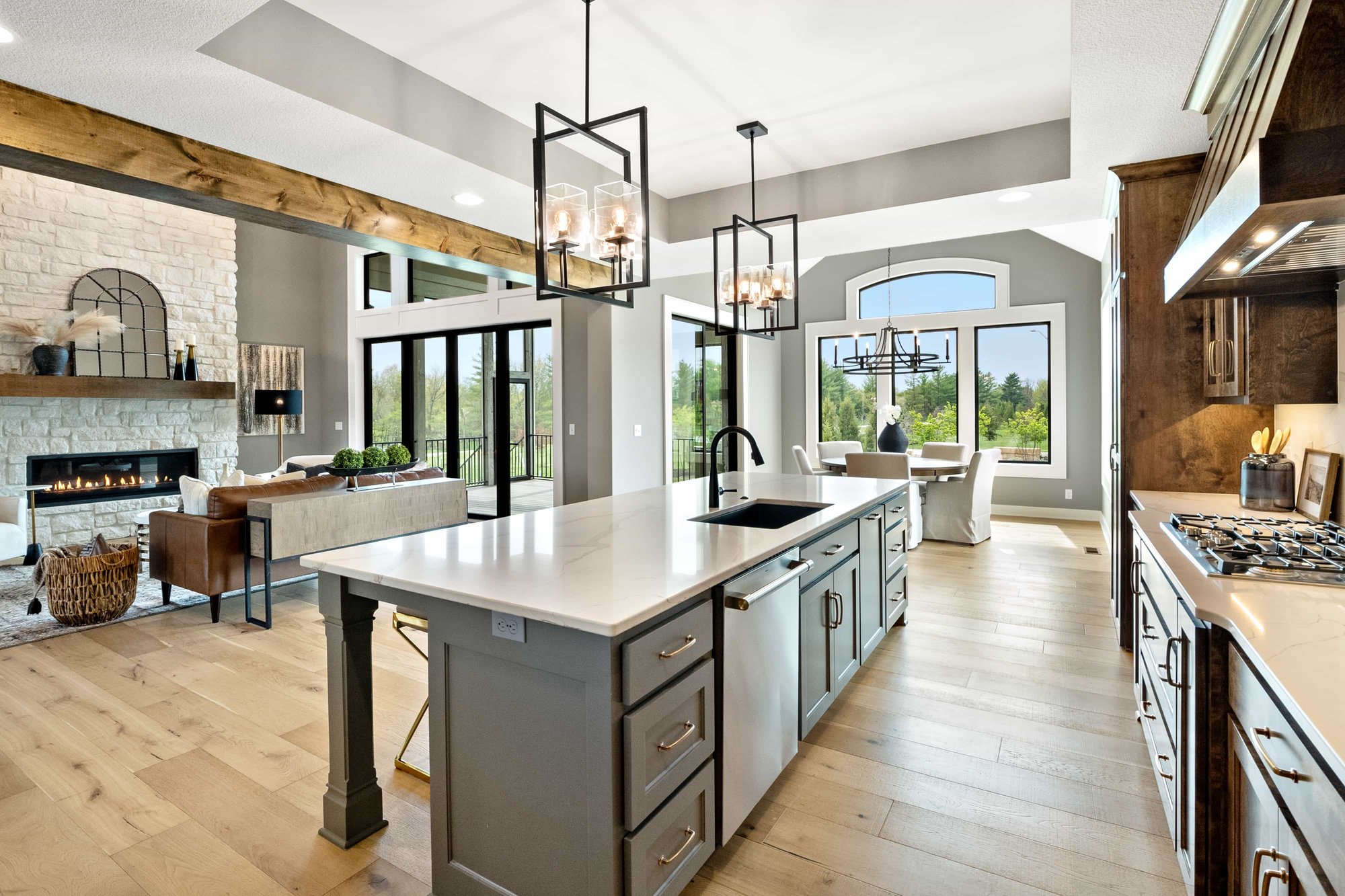 Open kitchen in a Dusty Rhodes Homes custom home in the Kansas City area, with a gray island and a living area beside a white brick fireplace.