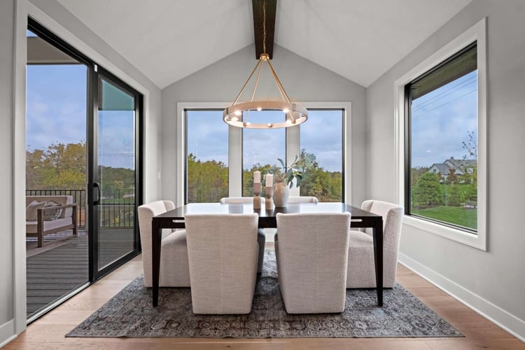 Image of a dining area connected to a covered patio with sliding glass doors and large windows in the room. 