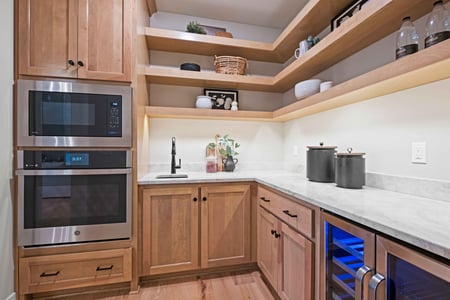 Image of a remodeled kitchen panty in Overland Park, Kansas, with a stainless steel microwave and oven and marble countertops. 
